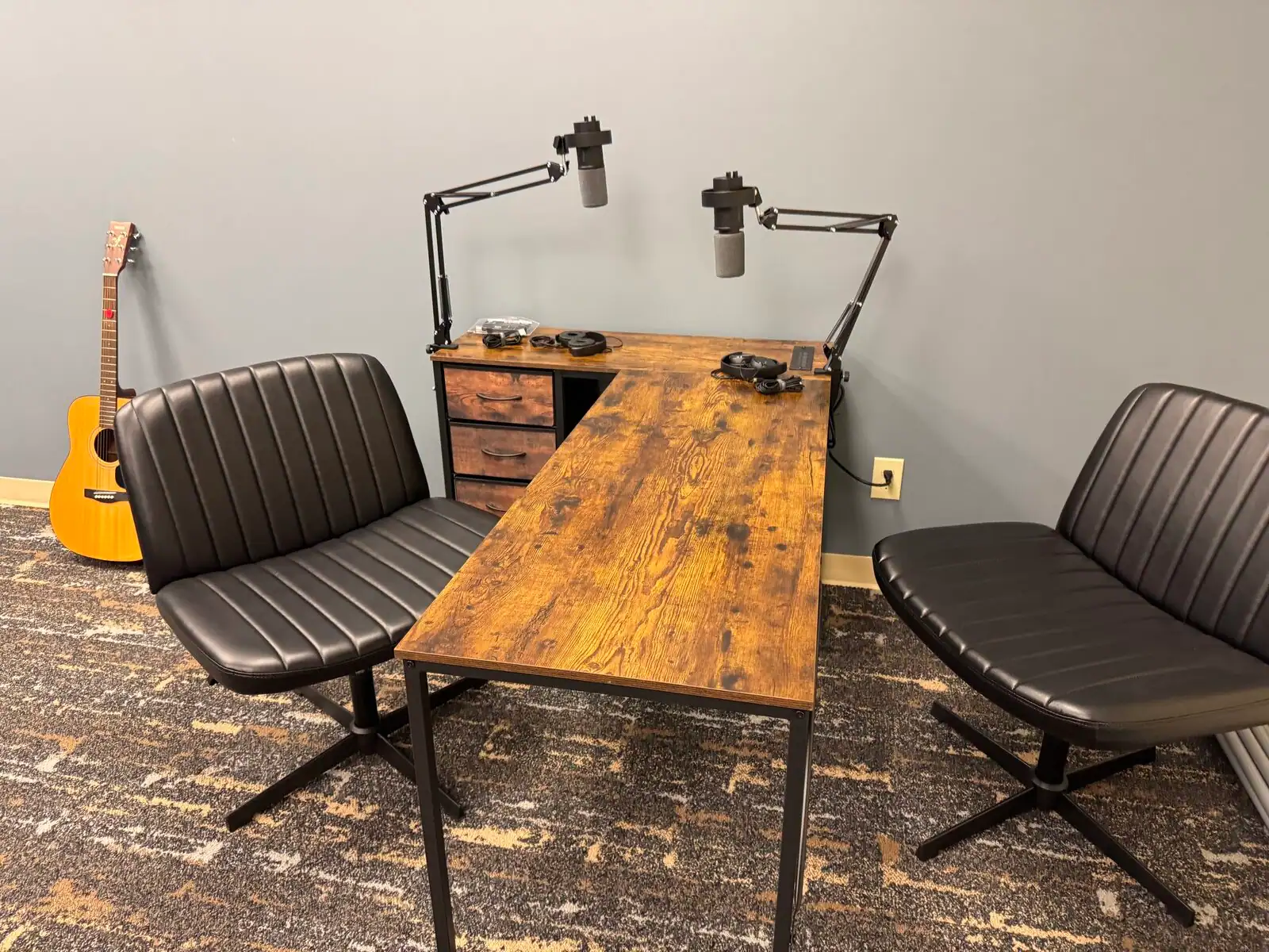 Podcast table, chairs, microphone arms, and guitar in a Tributary media room